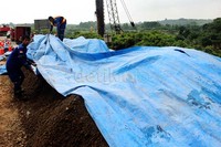 Petugas terpaksa menutupi material yang akan digunakan untuk pembaikan jalan tersebut dengan terpal agar tidak hanyut saat diguyur hujan.
