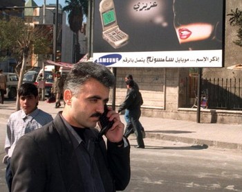 Seorang pria berdiri di depan iklan ponsel Samsung di Damaskus, Suriah. Foto ini diambil bulan Februari 2000.
