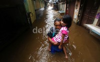 Seorang warga menyeberangi banjir dengan menggendong anaknya.