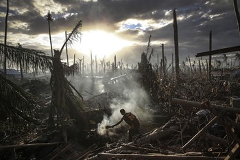     Seorang pria membakar sampah di Tanauan, Filipina November 2013. Tampak di sekitarnya adalah dampak dahsyat bencana topan Haiyan. (kredit foto: Dan Kitwood)