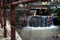 Sejumlah anak melompat ke dalam air. Meski kondisi kali tidak bersih, anak-anak tersebut tetap ceria.