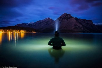 Fotografer Paul Zizka berdiri di dalam air sampai batas pinggangnya di danau Minnewanka, Taman Nasiona Banff, Alberta. Zizka tidak dibantu orang lain, dia menggunakan tripod atau sekadar meletakkan kamera di lokasi pemotretan terbaik. (kredit foto: Zizka.ca)