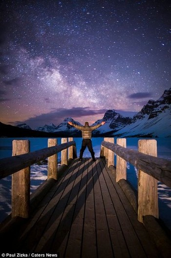Berdiri di dermaga diatas danau Taman Nasional Banff, Alberta dengan bintang-bintang yang bertaburan di langit. Ia lalu menjuluki fotonya ini sebagai Galactic Gateway. (kredit foto: Zizka.ca)
