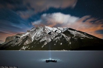 Dalam gambar ini fotografer berbaring di atas perairan beku danau Minnewanka, lalu senter mengarah ke langit malam yang indah. (kredit foto: Zizka.ca)