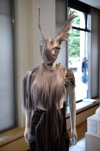 Karya lainnya menampilkan headpiece bentuk masker yang menutupi wajah. Yang satu ini terbuat dari rambut-rambut palsu dan tampak serasi dengan cape-nya.