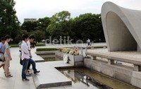 Pengunjung taman perdaiaman memperhatikan bunga dan tulisan di depan makam untuk memperingati korban bom atom pertama di dunia.