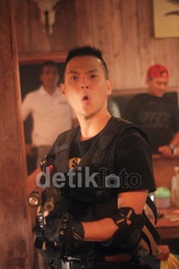Ernest berpose dengan senjata laras panjang, siap menembak.
