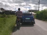 Sebuah mobil (Honda Civic) pasrah meminta bantuan motor (sepertinya Honda Revo) untuk bisa berjalan. Layaknya saat membantu sepeda motor yang mogok, mobil ini didorong menggunakan kaki oleh pengendara motor.
