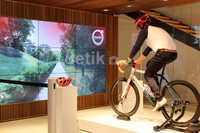Seorang pengunjung terlihat sedang mengayuh sepeda dengan monitor besar yang memperlihatkan jalanan di booth Volvo.
