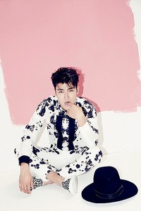 Berlatar belakang dinding putih dengan sentuhan cat pink, Siwon yang mengenakan busana hitam-putih berpose mengigit jarinya. (SMTOWN)