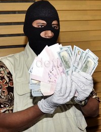 Seorang penyidik yang mengenakan topeng menunjukkan barang bukti uang dolar AS dan Singapura (SGD).