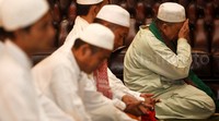 Hamzah salat berjamaah dengan mengenakan gamis dan berpeci putih. Dia duduk di shaf paling ujung.