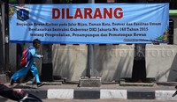 Seorang anak melintas di depan spanduk yang berisi larangan berjualan hewan kurban di jalur hijau di depan Kelurahan Kebon Kacang, Jakarta Pusat, Senin (7/9/2015).