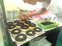 Seorang pegawai melumuri saus cokelat putih di atas setiap donat satu per satu.