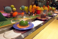 Beberapa jenis cake disajikan dalam piring kecil bertutup plastik mika dan berputar di conveyor belt atau ban berjalan mirip seperti restoran sushi.