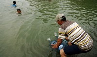 Seorang warga mengambil air sungai menggunakan galon.