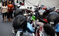 Para pejalan kaki melintas di depan puluhan motor yang diparkir di pinggir jalan.