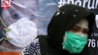 Para aktivis membentangkan spanduk bergambar seorang anak yang sedang memakai masker.