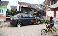Seorang anak bermain sepeda di depan rumah yang telah dipasangi garis polisi tersebut.