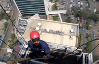 Seorang pekerja membersihkan kaca gedung dengan berbekal perlengkapan keamanan seperti gondola, helm dan tali.