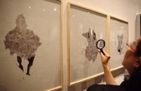 Seorang pengunjung melihat karya seni menggunakan kaca pembesar.