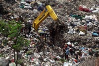 Para pemulung mencari sampah plastik di depan alat berat yang sedang melakukan pengerukan.