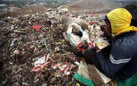 Seorang pemulung beristirahat sambil menyantap makanan di atas tumpukan sampah.