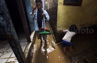 Seorang warga membersihkan lumpur di depan rumahnya.