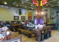 Interior SHSD kental dengan sentuhan tradisional seperti bangku dan meja dari kayu jati serta lukisan dan pajangan antik di dinding restoran.