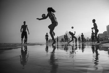 Foto hitam putih yang menampilkan kegiatan permainan bola yang dilakukan di pantai berlokasi Rio de Janeiro, Brasil. Karya fotografer Simone Monte. (kredit foto: Simone Monte/National Geographic)
