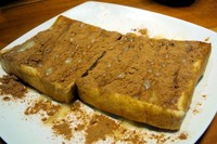 Roti panggang renyah dengan taburan susu bubuk cokelat dan siraman susu kental manis.