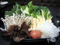 Satu wadah sayuran segar disajikan sebagai pendamping suki. Berisi jamur kuping, jamur enoki, selada, pocai, sawi putih, kangkung, dan daun bawang yang disajikan bersama telur rebus dan pad thai mentah.