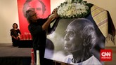 Seorang kerabat memasang kain ulos di foto almarhum Sitor Situmorang sebelum kedatangan jenazahnya. (CNN Indonesia/Safir Makki)