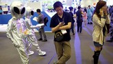 Pengunjung memakai ponselnya di dekat staf promosi yang memakai kostum alien di Global Mobile Internet Conference (GMIC) 2015 di Beijing, Tiongkok. (CNN Indonesia/Reuters/Kim Kyung-Hoon)