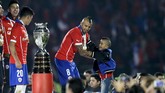 Arturo Vidal hendak menggendong putranya sebelum timnya diserahkan trofi Copa America 2015. Di partai final Chile mengalahkan timnas Argentina, 4 Juli 2015. (REUTERS/Jorge Adorno)