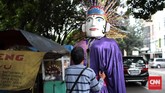 Seorang anggota pengamen ondel-ondel sedang memakaikan boneka ondel-ondel ke anggota lainnya yang bertugas mengenakannya. Profesi pemanggul Ondel-Ondel ini disebut Panjak.
