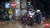 Tak hanya sepeda motor yang diangkut ke gerobak, pengendara pun ikut diangkut menembus banjir yang tak dapat dilalui kendaraan di bawah ruas Jalan Tol Bintara, Bekasi, Selasa (21/2). Baik pengendara motor maupun yang menarik gerobak harus berhati-hari karena banjir yang menerjang membawa arus. (CNN Indonesia/Safir Makki)