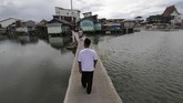 Warga melintasi jembatan penghubung pemukiman di Kampung Apung dengan daerah sekitar. Kampung Teko mulai tenggelam sejak tahun 2000-an karena industrialisasi dan pembangunan pemukiman mewah di sekitarnya. (Anadolu Agency/Eko Siswono Toyudho)