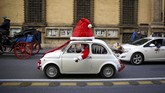 Seorang pria yang berpakaian seperti Santa Klaus membuyikan loncengnya sembari mengemudikan mobil Fiat 500 di kota Roma, Italla. (REUTERS/Alessandro Bianchi)