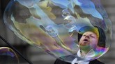 Seorang seniman jalanan menampilkan atraksi dengan gelembung sabun raksasa. Ia tampil di halaman Museum Sejarah Alam di London, Inggris. (REUTERS/Clodagh Kilcoyne)