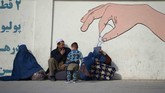 Perempuan Afghanistan yang mengenakan burka, seorang pria, dan seorang anak, duduk bersama di tepi jalan kota Mazar-i-Sharif. (AFP/Farshad Usyan)
