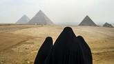 Wisatawan perempuan mengenakan kerudung hitam menatap Piramida Giza dari kejauhan. Mereka duduk di dataran tinggi Giza yang terletak di luar kota Cairo, Mesir. (AFP PHOTO / KHALED DESOUKI)