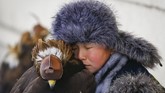 Seorang pemburu muda beristirahat dekat elang emas yang sudah dijinakkannya. Ia sedang mengikuti acara tahunan kompetisi berburu di Almaty, Kazakhstan. (REUTERS/Shamil Zhumatov)
