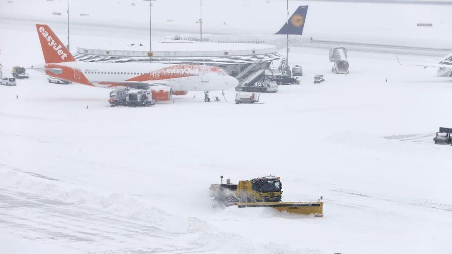 Seorang pria menyekop salju di samping pesawat EasyJet saat penutupan sementara di bandara Cointrin di Jenewa, Swiss, 1 Maret 2018. Gambar diambil melalui jendela. REUTERS / Pierre Albouy