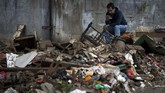 Seorang pria menggunakan ponselnya seraya duduk di tempat yang sekitarnya sampah berserak usai banjir surut di kawasan bantaran Sungai Ciliwung, Jakarta, 8 Februari 2018. (AFP PHOTO / BAY ISMOYO)