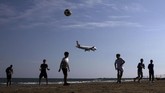 Anak-anak bermain sepak bola di pantai sementara pesawat terbang sedang mendarat di Bandara Internasional Larnaca, Siprus. (REUTERS/Yiannis Kourtoglou)