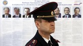 Seorang polisi berjaga, sementara di belakangnya tampak foto dan keterangan tujuh kandidat dalam pemilihan presiden kali ini. Presiden petahana, Vladimir Putin pun ikut dalam kontestasi ini, 18 Maret 2018. (REUTERS/Eduard Korniyenko)