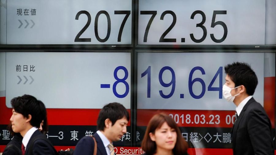 A man looks at a mobile phone in front of an electronic board showing Japan's Nikkei average outside a brokerage in Tokyo, Japan, March 23, 2018.  REUTERS/Toru Hanai