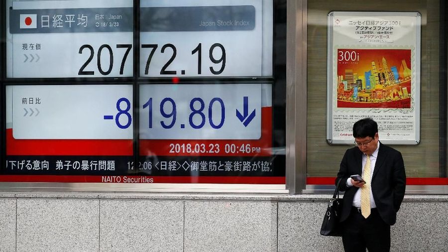 A man looks at a mobile phone in front of an electronic board showing Japan's Nikkei average outside a brokerage in Tokyo, Japan, March 23, 2018.  REUTERS/Toru Hanai