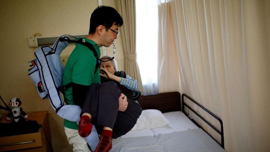 Seorang juru kunci yang memakai alat bantu gerak 'Muscle Suit' membawa seorang penduduk dari tempat tidur ke kursi roda di rumah perawatan Shin-tomi di Tokyo, Jepang, 5 Februari 2018. REUTERS / Kim Kyung-Hoon